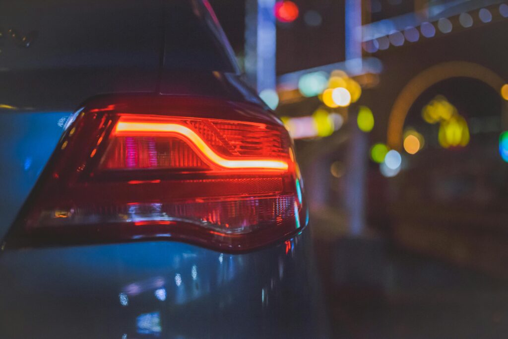 Night time photograph of a sedan tail light with the city lights in the background