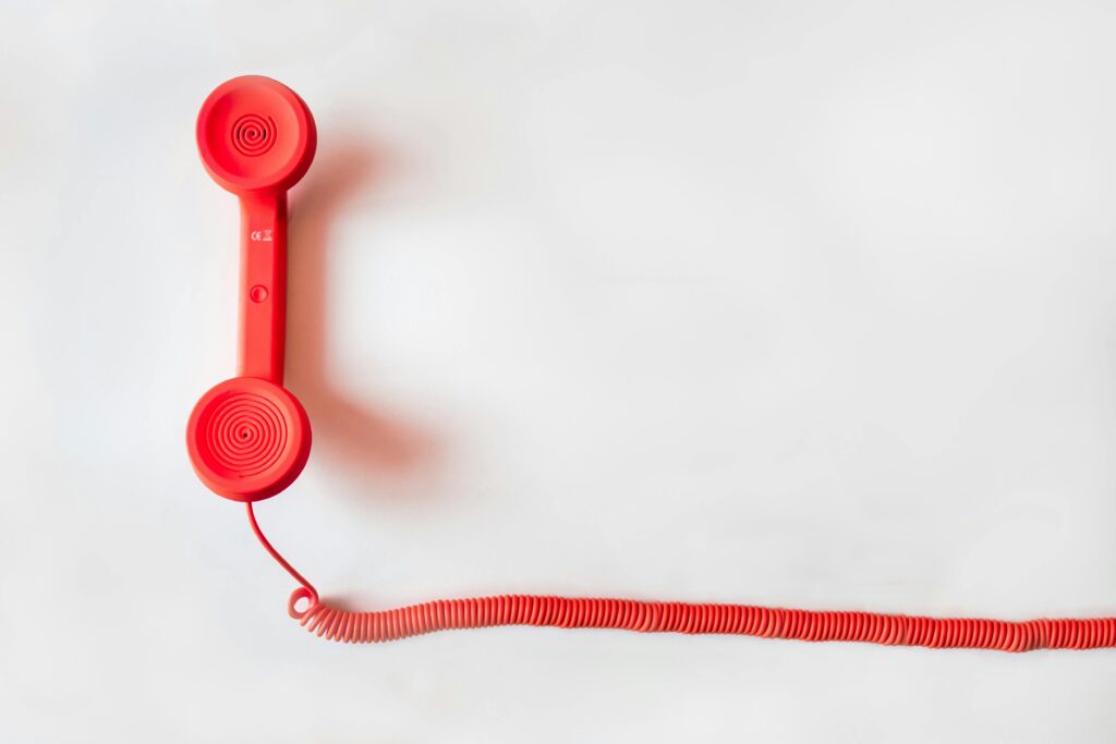 minimalistic photograph of a red, corded desk phone laying on a white surface