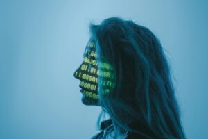 An artistic photograph of a woman with matrix code displayed across her face. This is to display the relationship between humans and artificial Intelligence